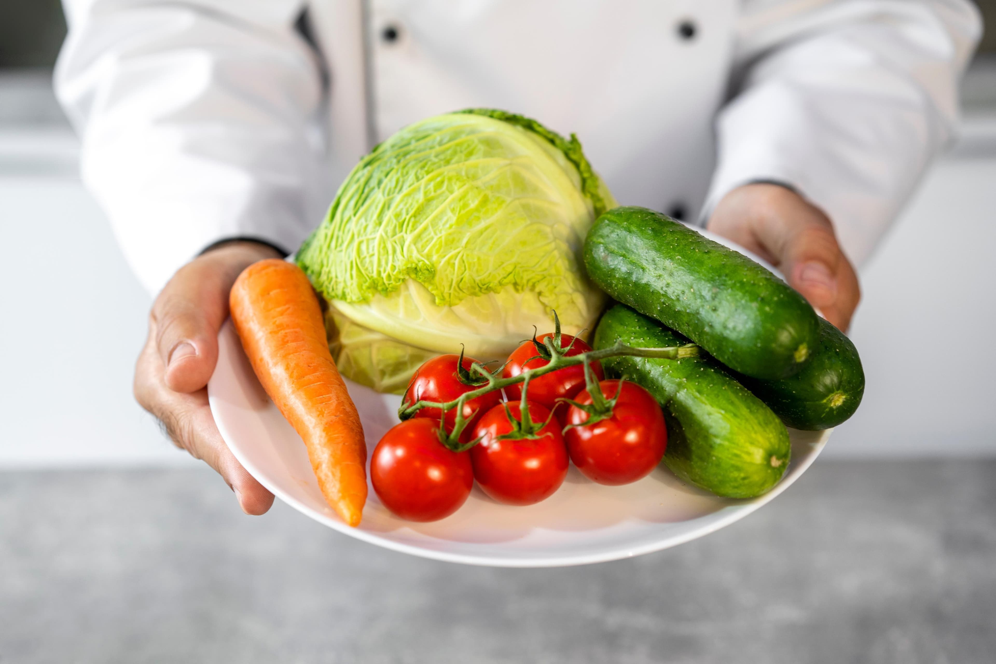 Chef présentant une assiette de légumes frais — chou, carotte, tomates, concombres